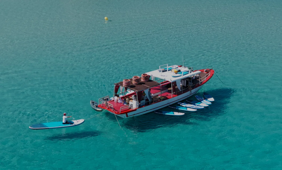 Top-down aerial view of Salvador Ibiza in Cala Comte with a guest paddleboarding near the stern